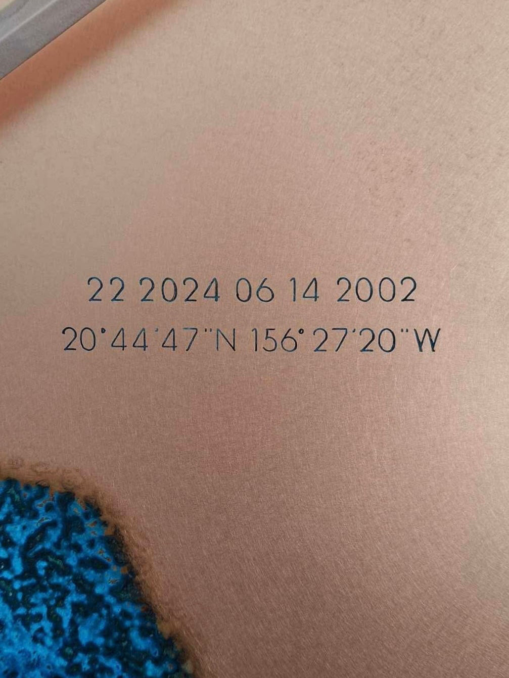 A close-up picture of a Blue Patina Copper “Half Time” clock engraved with coordinates and date printed on it.