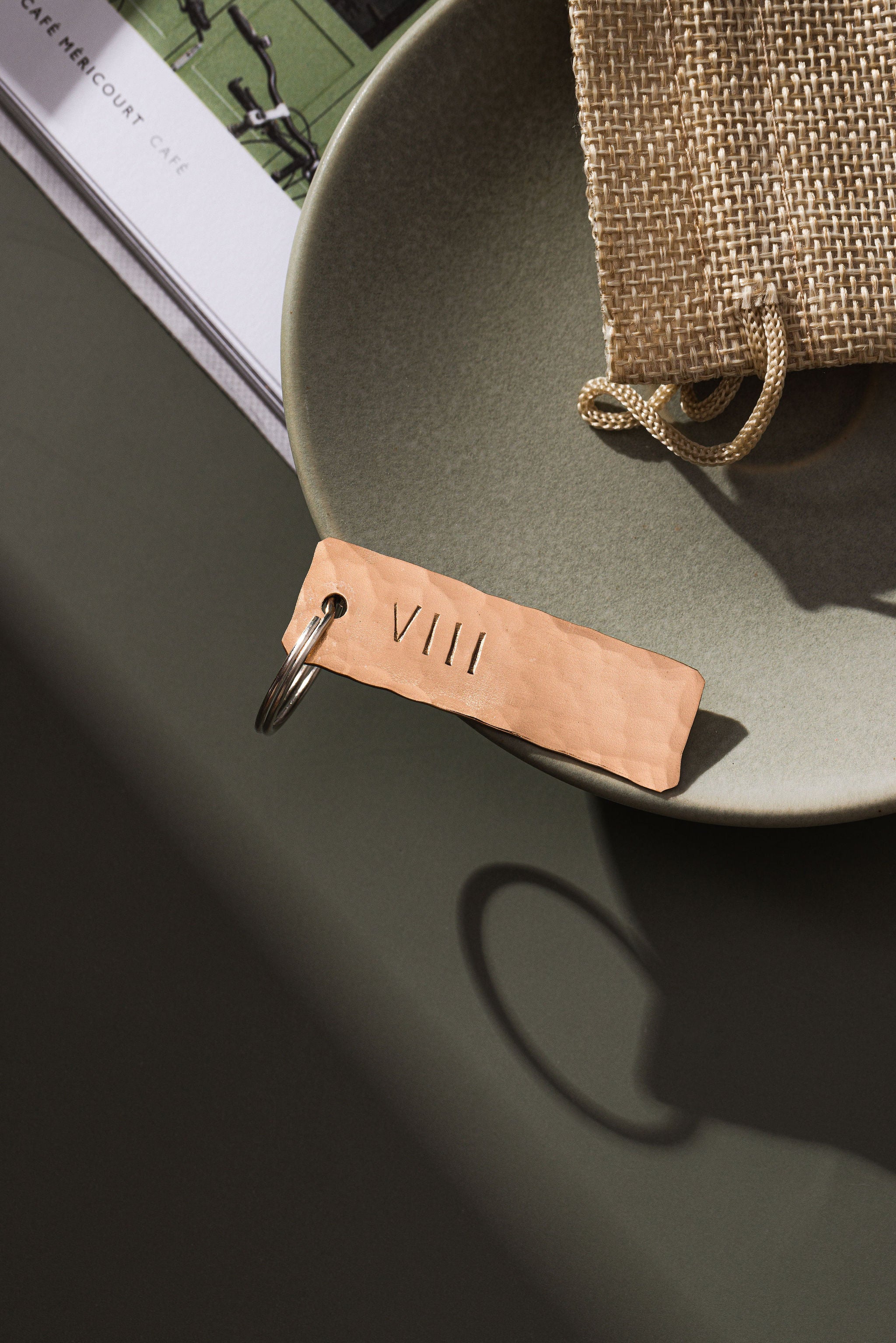 A keyring made from bronze that has been planished and engraved with the roman number symbols VIII which is the symbol for the number 8. The bronze keyring is on a moss green surface. The keyring is made by Empire Copper.